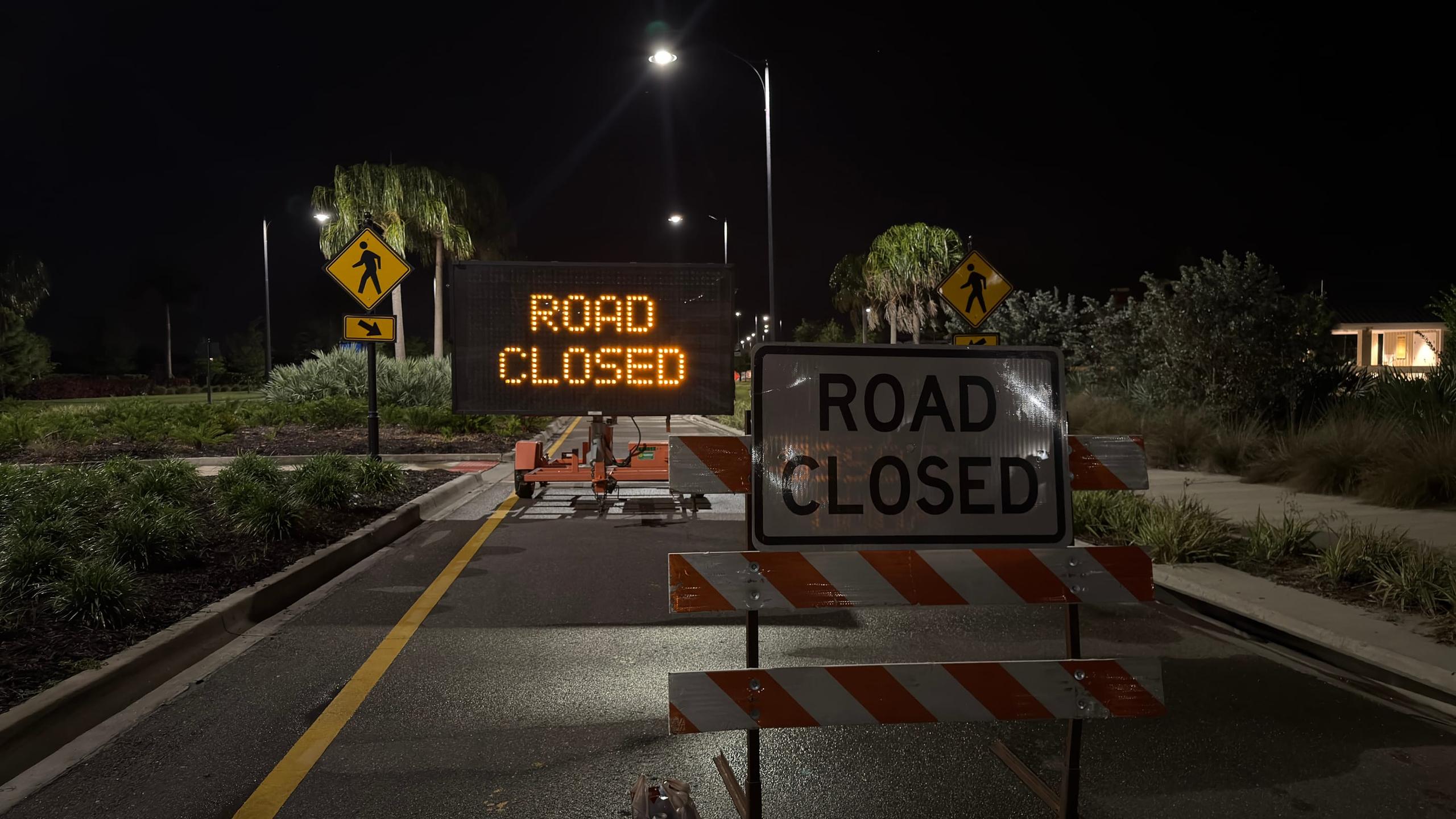 Road-closed barricades and a lit warning sign across an empty street at night