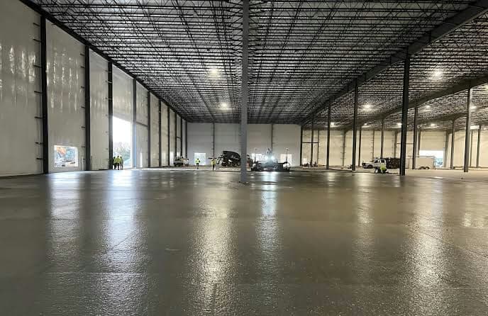 Sealed concrete floor slab inside a large industrial warehouse under construction