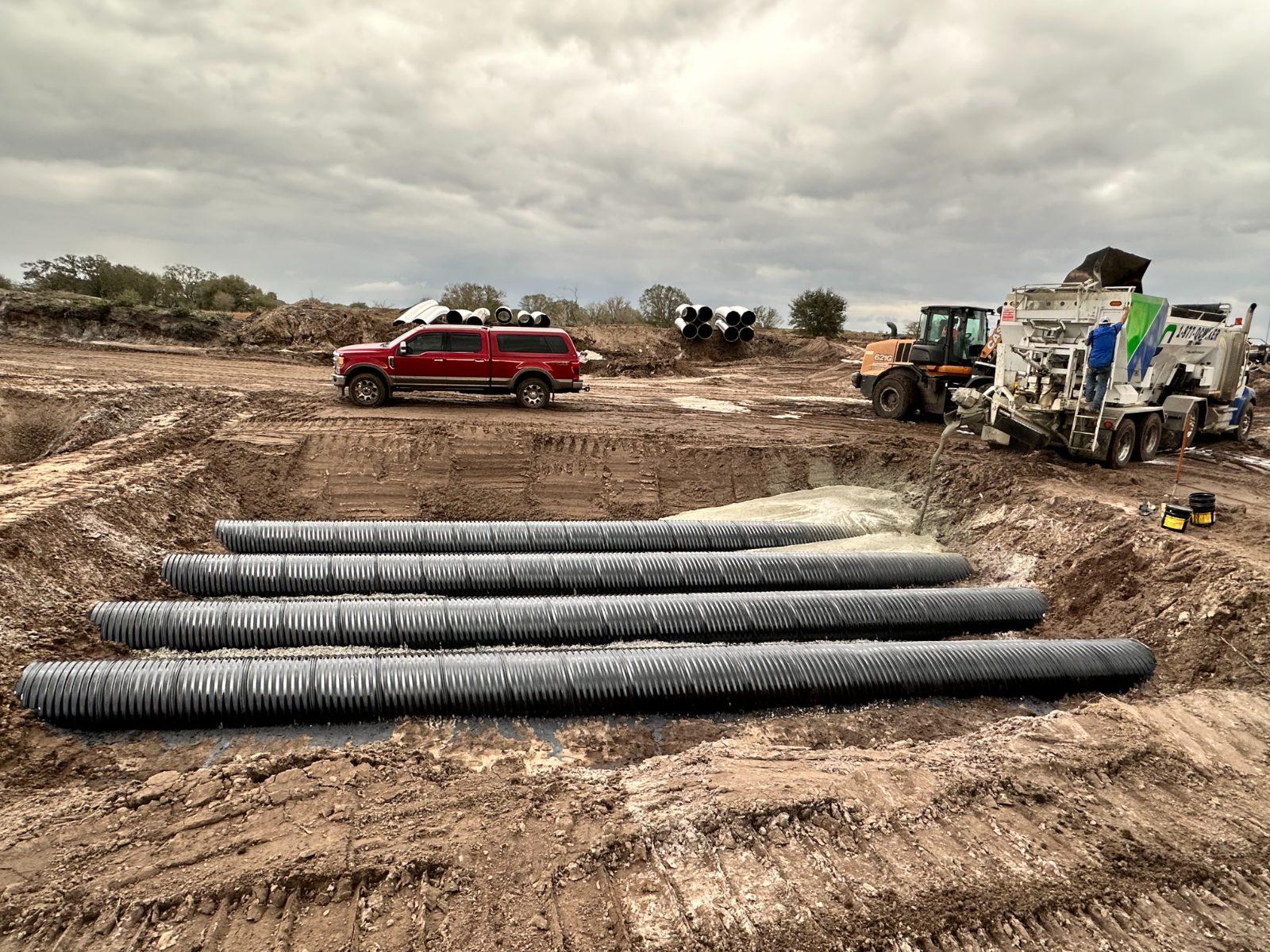 Culvert pipe staged on a rural site beside a Quality-Crete mixer