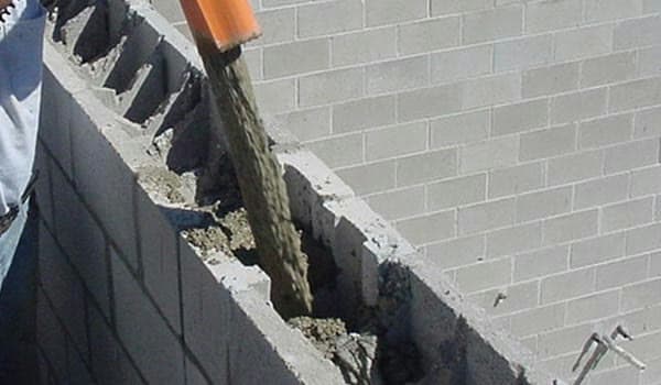 Concrete being poured through a hose into the open cores of a block wall under construction