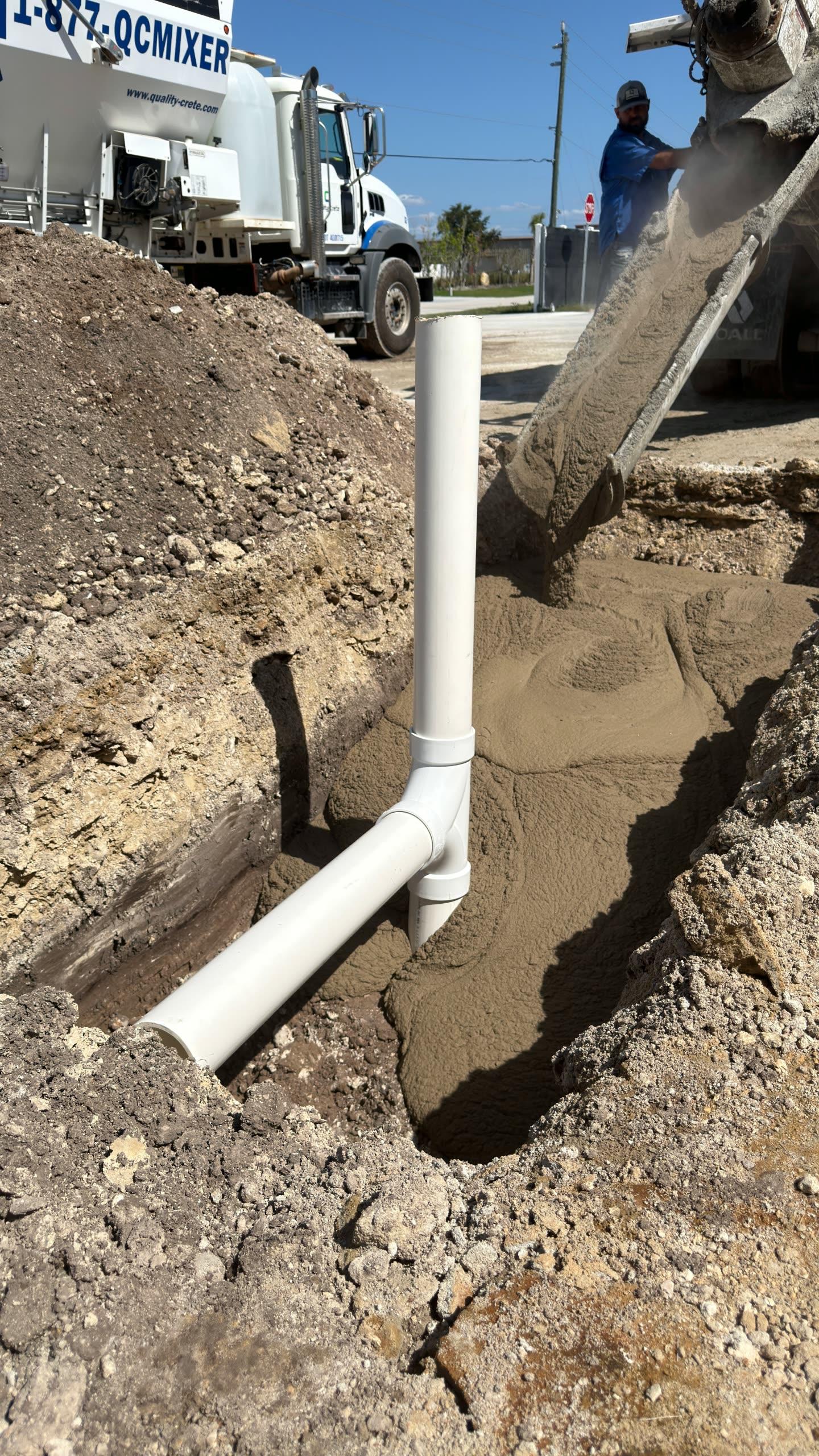 Quality-Crete mixer truck discharging fast setting flowable fill into a utility trench around a PVC pipe fitting