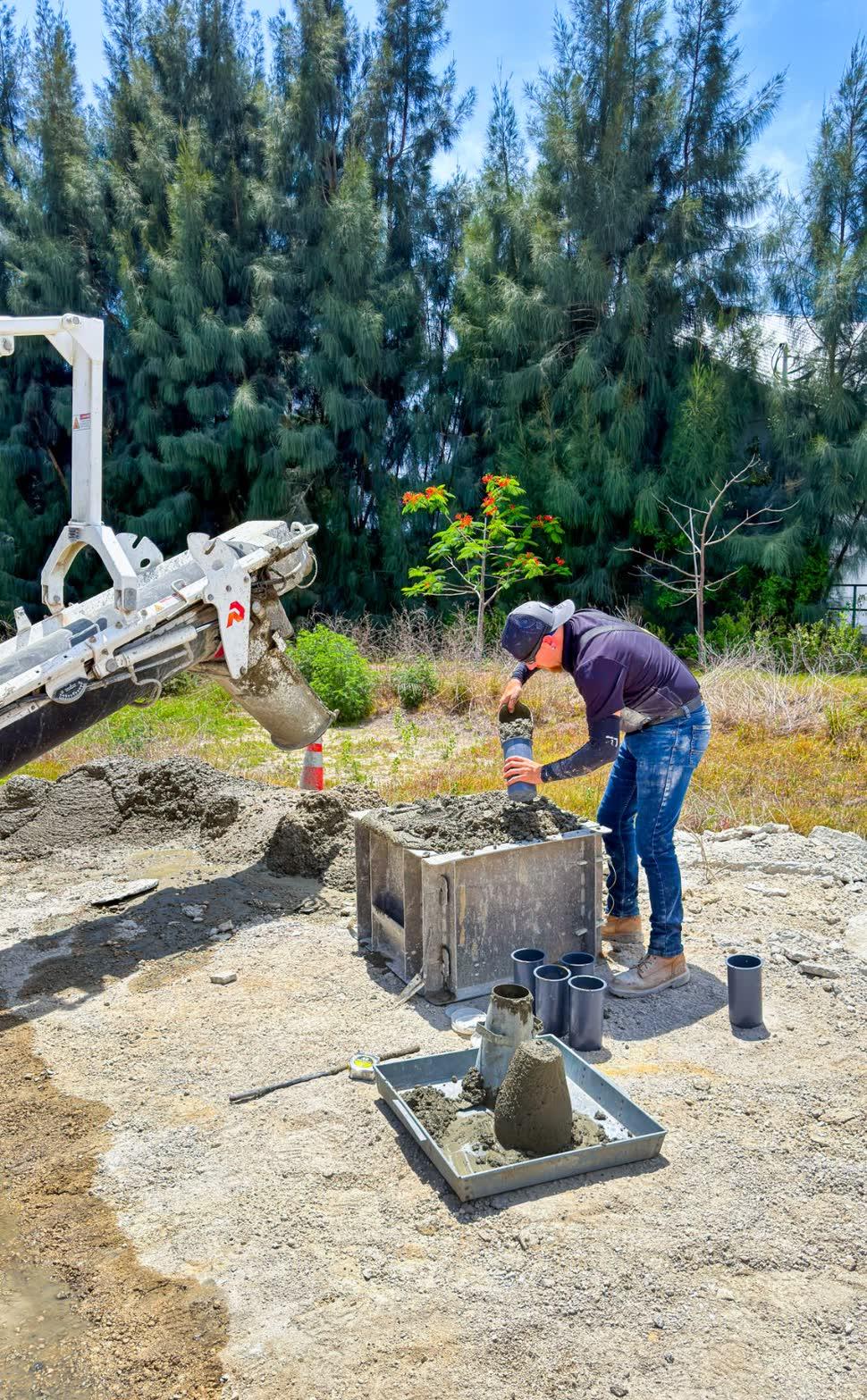 Technician filling test cylinders from a volumetric mixer chute beside a slump test